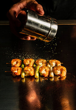 Chef seasoning prawn skewers on a teppanyaki grill