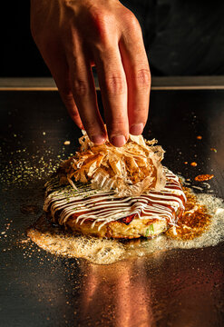 Chef hand placing bonito flakes on hot okonomiyaki