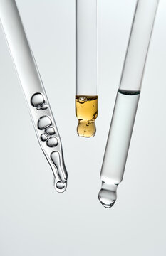 Three glass pipettes with different liquids on light gray backdrop.