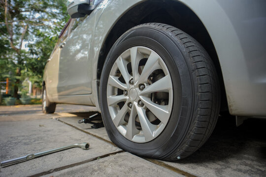 A car with a flat tire that still has a nail embedded in the tread. The tire-changing process is underway, with tools scattered nearby; this image depicts vehicle maintenance and automotive service.