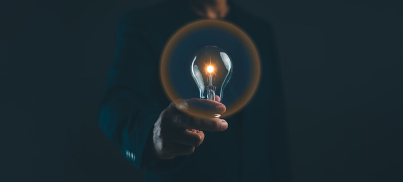 A hand holds a glowing light bulb in the dark, symbolizing innovation and bright ideas.