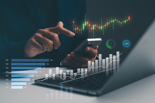 A person interacts with a smartphone while analyzing digital financial charts and graphs projected above a laptop.