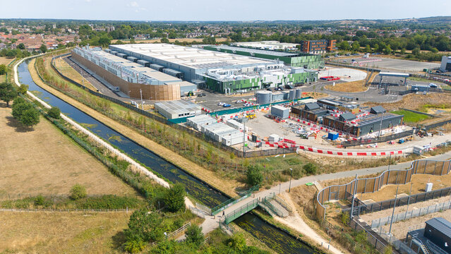 Aerial view of a hyperscale data center complex with air handling units and chillers, adjacent to a canal and green fields in Hereford, England, United Kingdom.