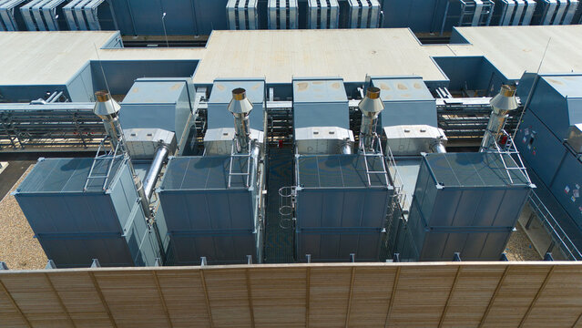Aerial view of a hyperscale data center rooftop featuring large industrial air handling units and chillers with metal ventilation stacks in Hereford, England, United Kingdom.