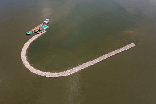 Aerial view of a U-shaped stone breakwater in the Danube river with a barge and dredger working on the construction of the river structure in Belegis, Vojvodina, Serbia.