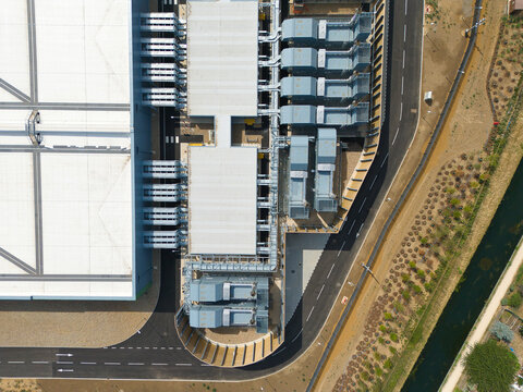 Aerial view of a hyperscale data center with rows of air handling units and industrial chillers, adjacent to a paved road and canal in Hereford, England, United Kingdom.