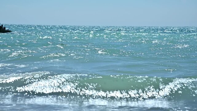 Waves gently crash on sandy beach, sunlight sparkling on water surface