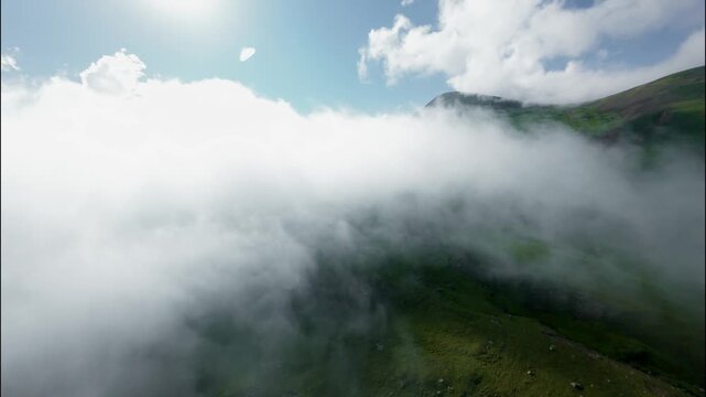 Aerial view of clouds rolling over green hills under bright sunlight