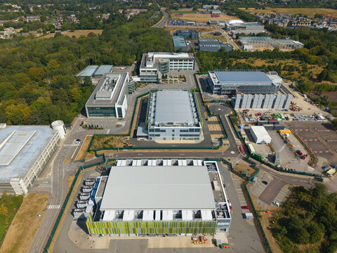 Aerial view of a modern data center complex with server buildings, containerised diesel generators, and cooling infrastructure for AI in Harlow, England, United Kingdom.
