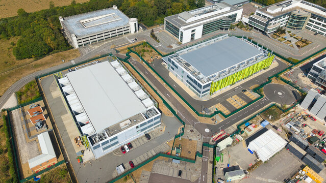 Aerial view of a modern data center facility featuring containerised diesel generators and cooling infrastructure for AI operations in Harlow, England, United Kingdom.
