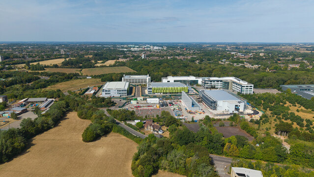Aerial view of a data center with containerised diesel generators and cooling infrastructure for AI, set among green fields and industrial buildings in Harlow, England, United Kingdom.