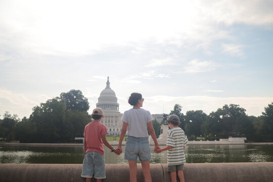 Family group. A mother and her two children. Standing with backs to the viewer. Holding hands while observing the iconic united states capitol building and reflecting pool