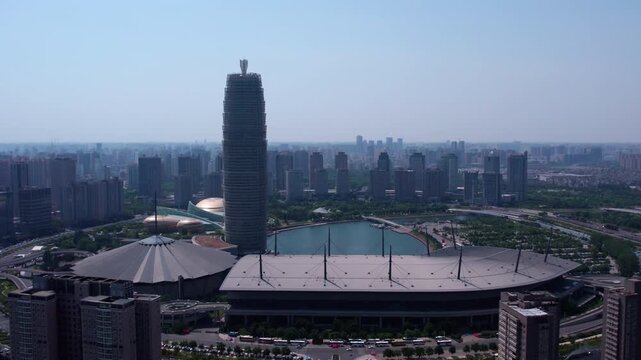 A high-angle aerial shot of a modern urban area featuring a central lake, distinctive skyscraper, and large public facilities under clear sky.