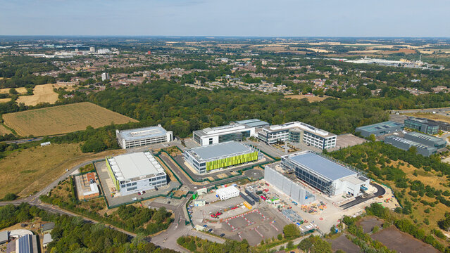Aerial view of a modern data center facility with containerised diesel generators and cooling systems for AI infrastructure, set among green trees in Harlow, England, United Kingdom.