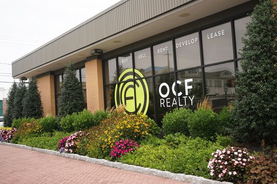 Margate City, New Jersey, U.S.A - Aug 17, 2026 - OCF Realty office featuring large glass windows with service labels and colorful landscaped surroundings