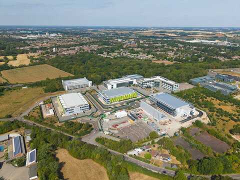 Aerial view of a modern data center facility featuring containerised diesel generators and cooling systems for AI infrastructure, surrounded by green landscape in Harlow, England, United Kingdom.