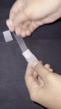 Close-up of a woman filing and buffing her fingernails with a glass nail file.