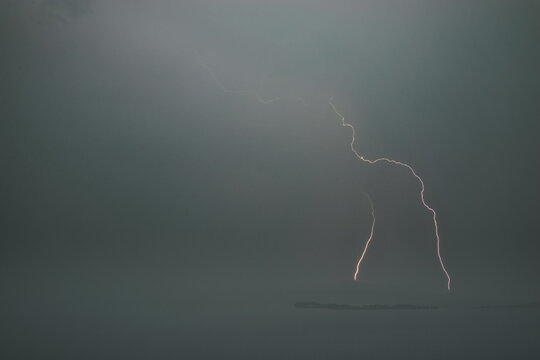 Dramatic lightning bols striking through dark stormy sky over water in a minimalist coastal landscape scene