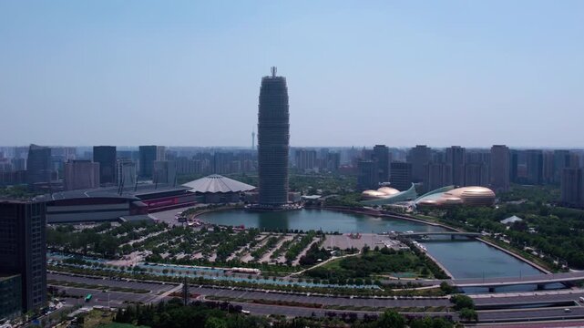 A daytime aerial view of a modern urban district featuring a tall landmark skyscraper, surrounding water bodies, and architectural complexes.