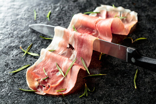 Sliced prosciutto and knife on a stone table.