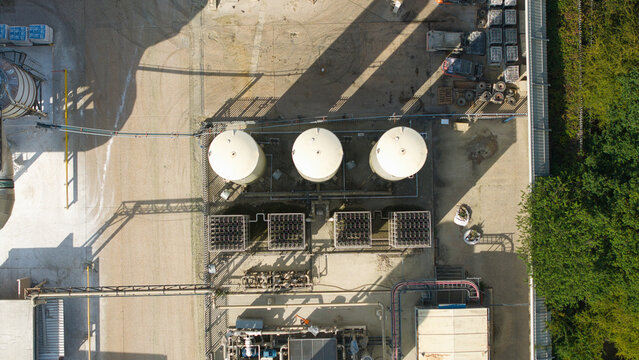 Aerial view of cryogenic storage tanks and gas vaporization systems at a glass manufacturing facility with industrial piping and concrete surfaces in Harlow, England, United Kingdom.