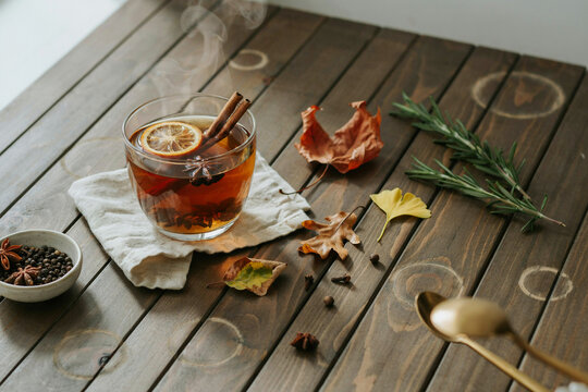 A steaming hot festive autumn beverage featuring fragrant cinnamon sticks a dried orange slice and star anise in a clear glass resting on a crisp white linen napkin on a rustic wooden surface