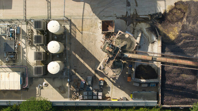 Aerial view of cryogenic storage tanks and gas vaporization systems at a glass manufacturing facility with conveyor belts and raw material piles in Harlow, England, United Kingdom.