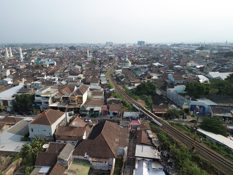 Aerial view of the dense residential neighborhood with a railway track running through the urban landscape, featuring traditional rooftops and mosques in Blimbing, East Java, Indonesia.