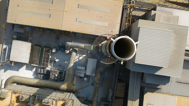 Aerial view of the O-I Glass Limited manufacturing facility featuring industrial rooftops, a large chimney stack, and complex ventilation piping in Harlow, England, United Kingdom.