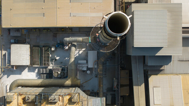 Aerial view of the O-I Glass Limited facility showing the industrial chimney stack, ventilation systems, and rooftops at the glass manufacturing plant in Harlow, England, United Kingdom.