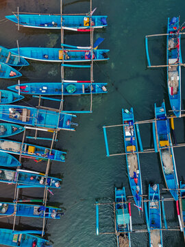 Aerial view of blue fishing boats with wooden outriggers moored in the clear water at Baron Beach in Yogyakarta, Special Region of Yogyakarta, Indonesia.