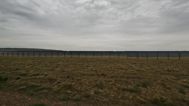 View from car driving past expansive solar farm under cloudy sky