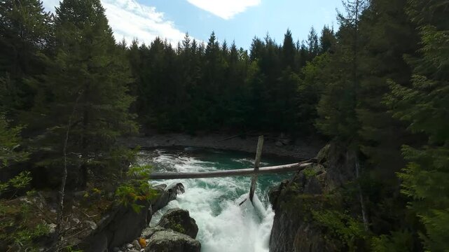 A dynamic forward moving aerial shot tracks from a natural cross log jam pile, sweeping around a winding river bend over powerful white water rapids on a beautiful summer day.