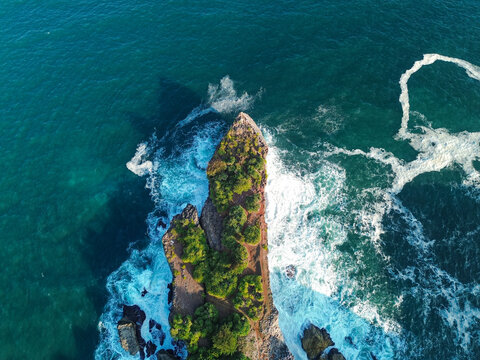 Aerial view of Baron Beach with rocky cliffs, lush vegetation, and turquoise ocean waves crashing against the shore, Yogyakarta, Special Region of Yogyakarta, Indonesia.
