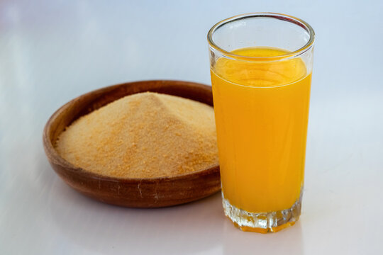 Orange flavored drink powder heap in wooden bowl beside filled glass of orange juice on white background. Instant fruit juice mix prepared for summer refreshing drink.
