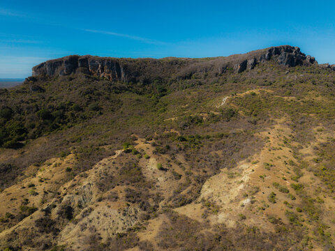 Aerial view of French Mountain featuring rugged rocky cliffs, dry savanna vegetation, and rolling hills under a clear blue sky in Antsiranana, Diana, Madagascar.