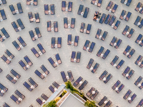 Aerial view of rows of sun loungers and umbrellas arranged on the white sand of a beach with a building corner and lush greenery in Ksamil, Vlore County, Albania.