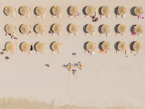 Aerial view of Kroreza Beach featuring rows of straw parasols and sun loungers with people relaxing on the sandy shore in Sarande, Vlore County, Albania.