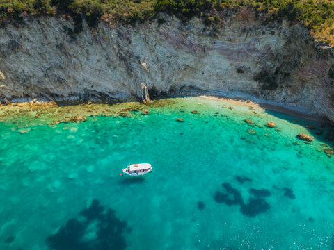 Aerial view of a small white boat floating in the clear turquoise waters of the Ionian Sea near the rocky cliffs of Kepi i Qefalit in Sarande, Albania.