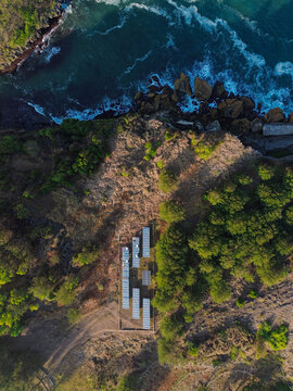 Aerial view of solar panel array installed on a cliff edge overlooking the turquoise waters and rocky coastline of Baron Beach in Yogyakarta, Special Region of Yogyakarta, Indonesia.