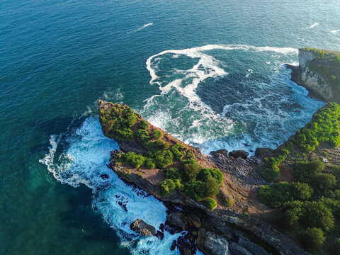 Aerial view of Baron Beach with rocky cliffs, lush green vegetation, and crashing waves in the turquoise ocean water in Yogyakarta, Special Region of Yog, Indonesia.