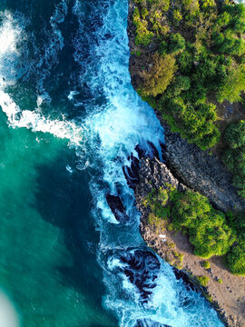 Aerial view of Baron Beach with turquoise waves crashing against the rugged rocky coastline and lush green vegetation in Yogyakarta, Special Region of Yogyakarta, Indonesia.