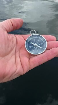 Navigating sea. Compass in hand at sea. Tourist compass for orientation in ocean. Adventure exploration in high seas. Map reading and land navigation concept. Orient on maps in sea. Boat trip on sea. 