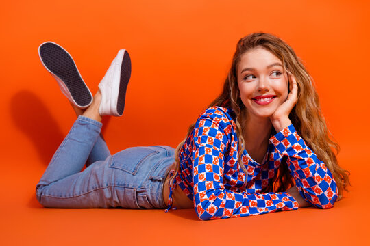 Charming smiling woman in casual checkered outfit relaxing on orange background, vibrant youthful energy and trendy style