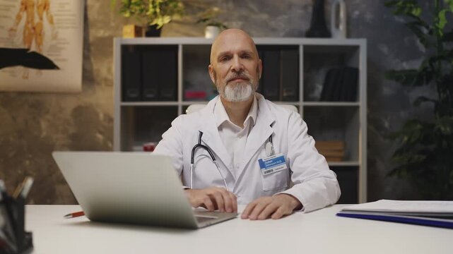 Portrait of smiling male physician working on laptop in his medical office