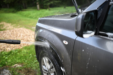 Fototapeta premium High pressure water jet washing dirty car body and front fender outdoors, concept of vehicle cleaning, detailing and home car maintenance.