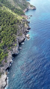Aerial video of a dramatic rocky cliff along the coastline of Mallorca, Spain, overlooking the deep blue Mediterranean Sea beneath clear skies, 4k.