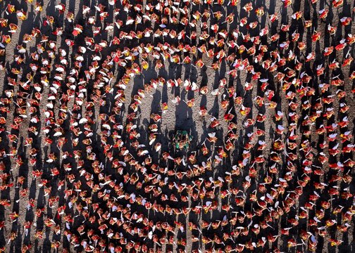 Aerial view of dancers in traditional red and gold costumes performing a circular formation on the sandy beach at Pantai Boom Marina in Banyuwangi Sub-District, East Java, Indonesia.