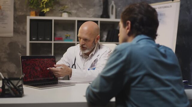 Hematologist explains blood test results on laptop to male patient in clinic