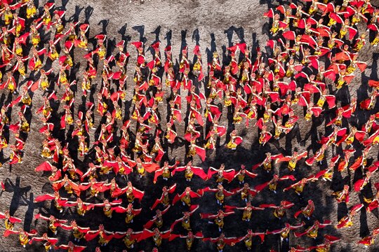 Aerial view of a large group of dancers in traditional red and gold costumes performing on a sandy ground at Pantai Boom Marina, Banyuwangi Sub-District, East Java, Indonesia.